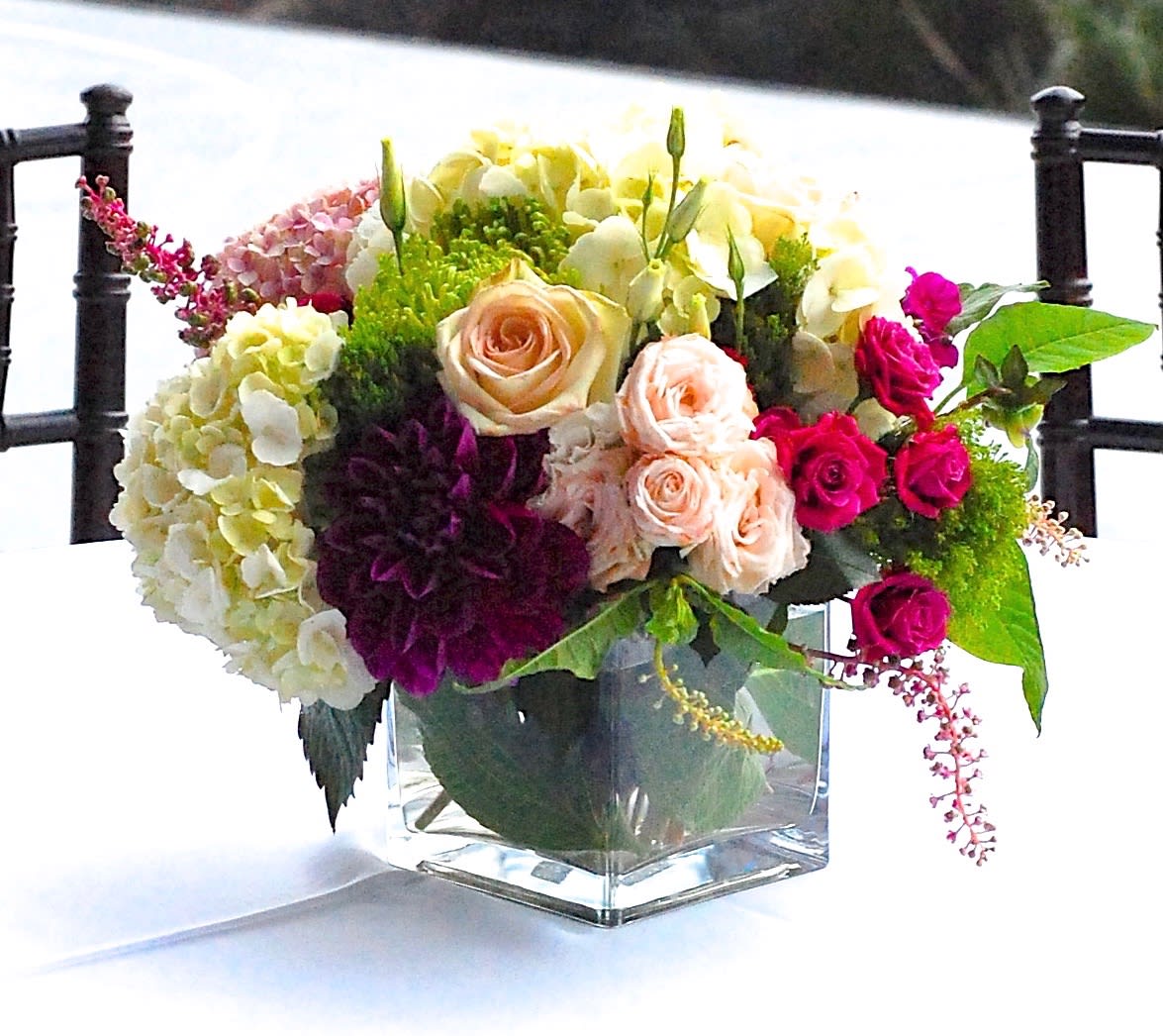 Mixed bouquet of roses, hydrangeas, and orchids in a clear square vase