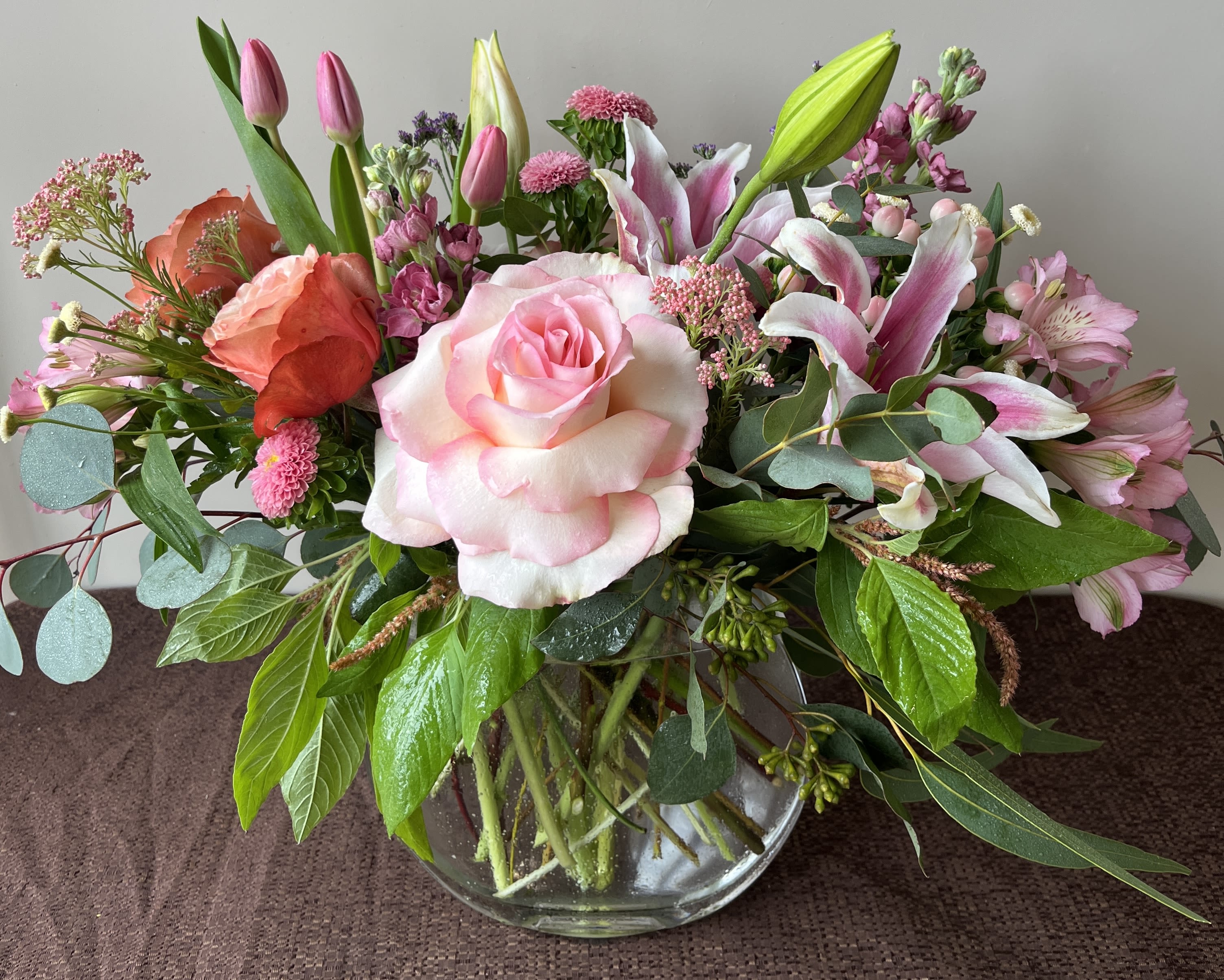 Mixed bouquet of pink roses, lilies, and tulips in a glass vase
