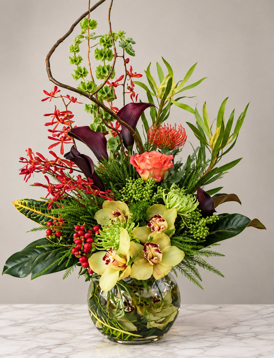 Tropical floral arrangement in a glass vase with orchids, calla lilies, and red accents