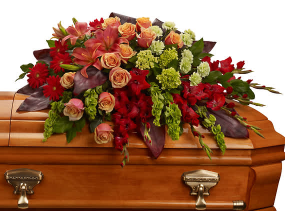 Floral casket spray with red, peach, and green blooms on a wooden casket