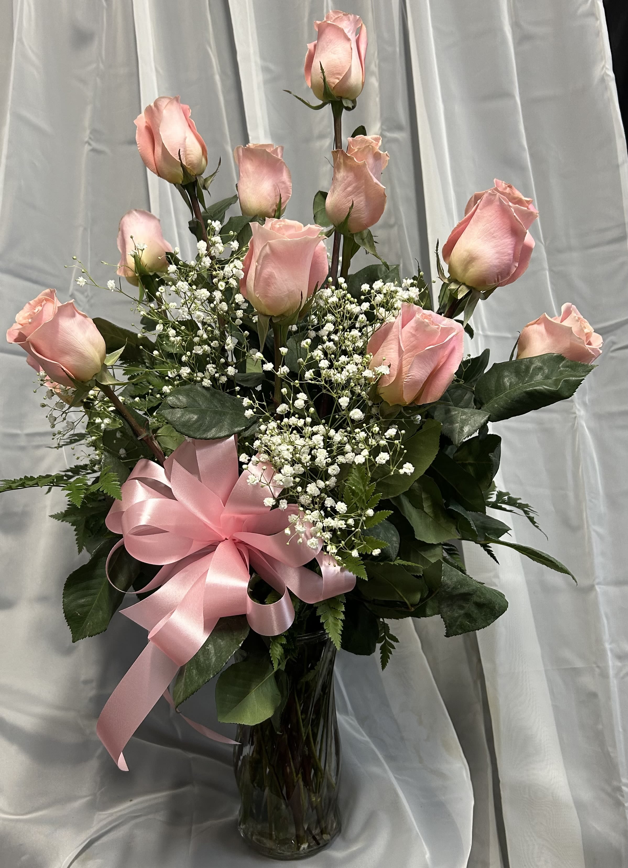 Pink roses in a glass vase with baby's breath and a pink ribbon