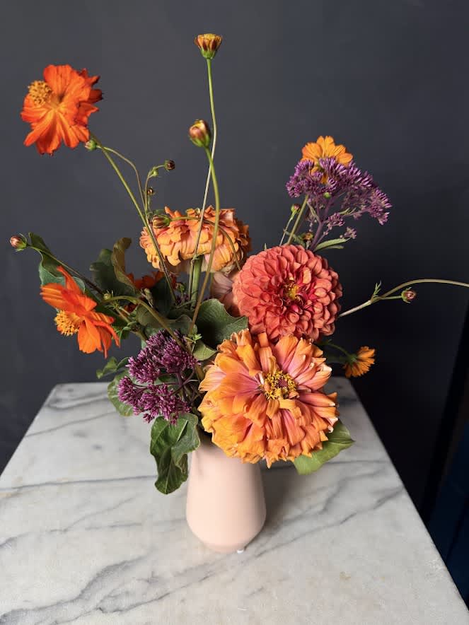Orange and pink flowers arranged in a pale vase