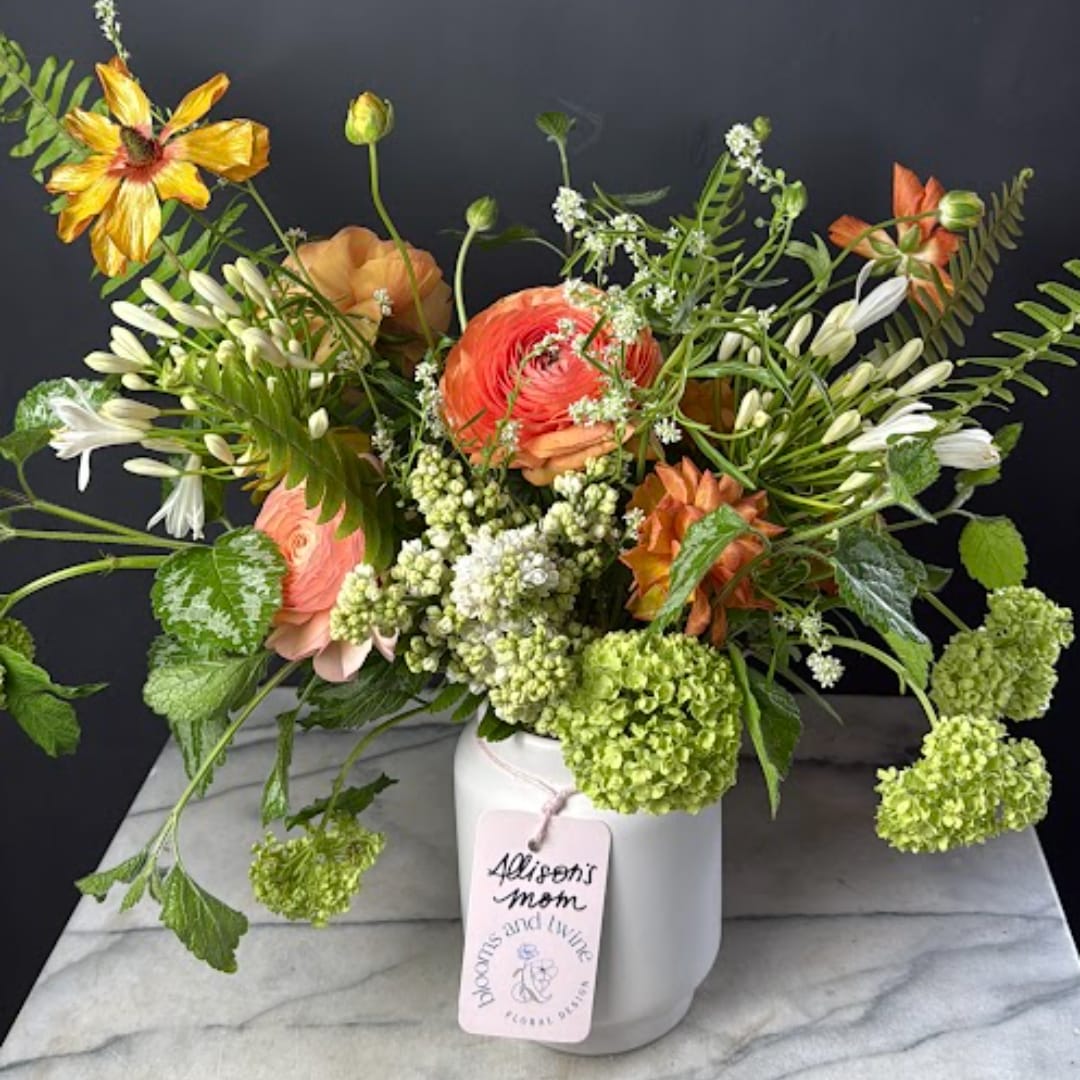 Mixed bouquet in a white vase with coral, white, and green blooms