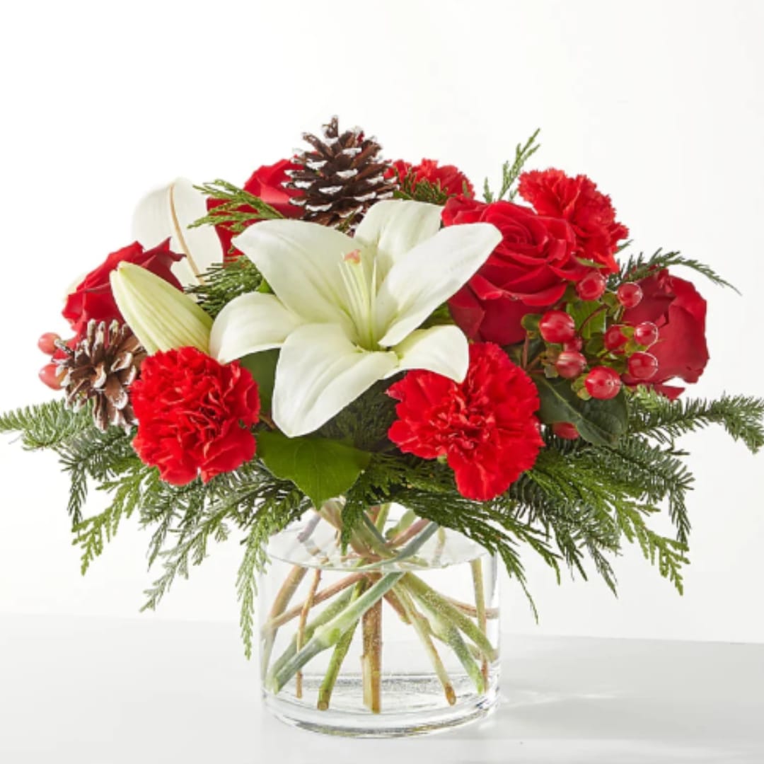 Red roses and carnations with a white lily in a glass vase