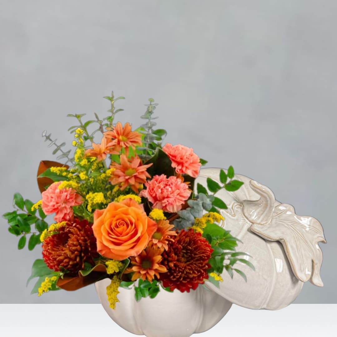 Orange and pink flowers arranged in a white pumpkin-shaped container