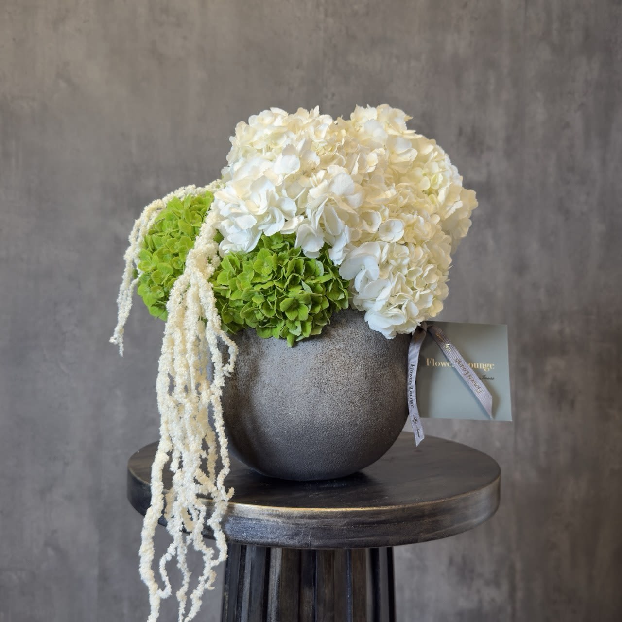 Ivory Balance - A clean and elegant arrangement of white and green hydrangeas, accented with soft cascading texture, designed in a modern ceramic vase. Minimal, fresh, and beautifully balanced, this piece brings calm sophistication to any space. Perfect for thoughtful gifting or refined interiors. Custom greeting card included.