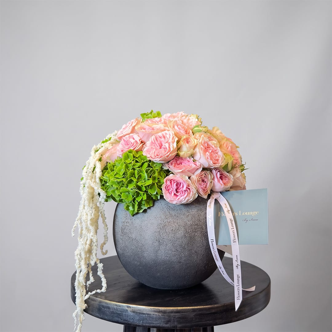 Pink roses and green hydrangea in a dark round vase with trailing white flowers