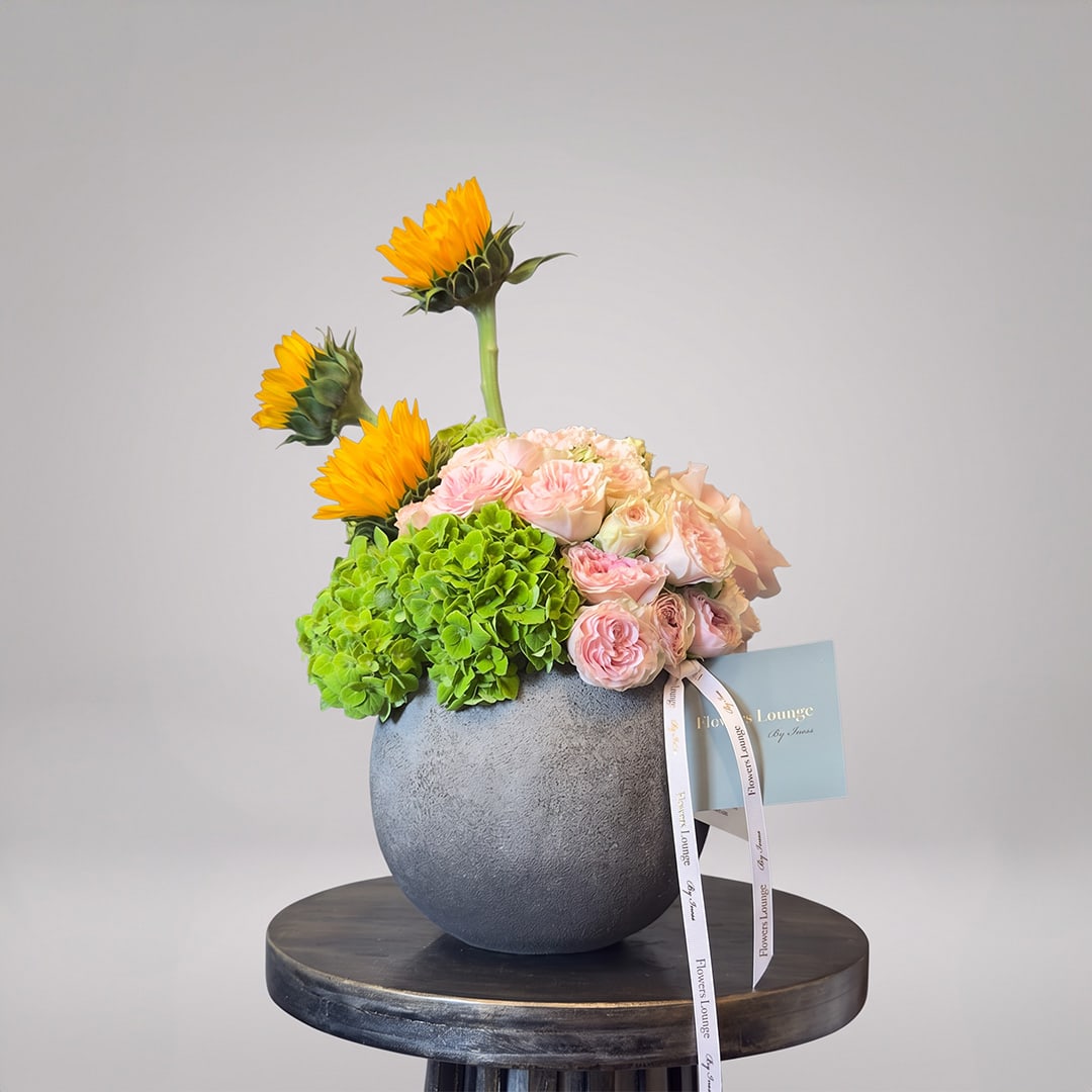 Mixed bouquet with sunflowers, pink roses, and green hydrangeas in a gray vase