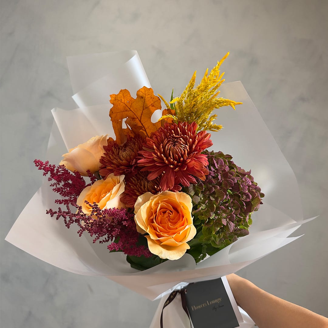 Bouquet of orange roses, burgundy mums, and purple hydrangea in white wrap