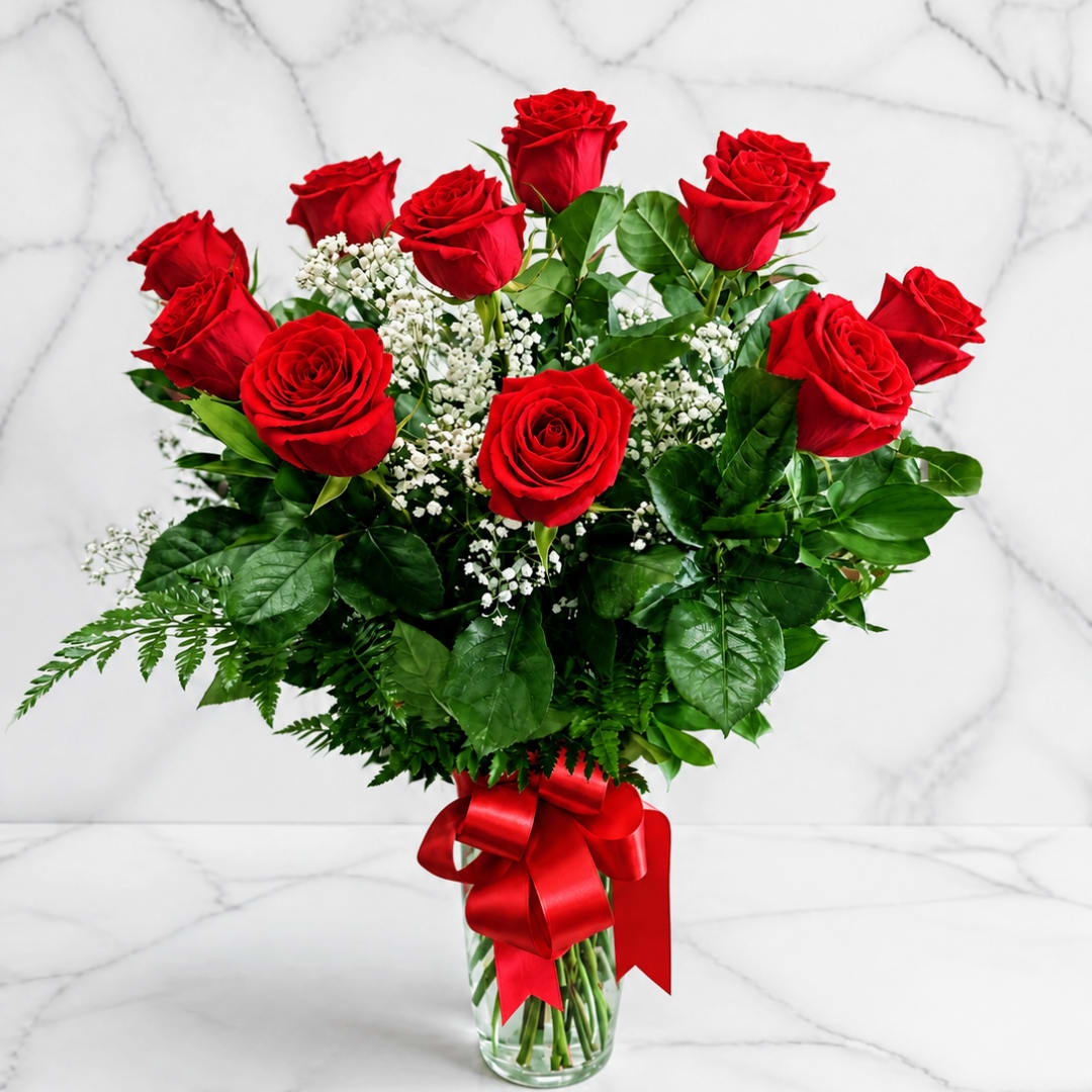 Red roses in a clear glass vase with baby's breath and a red ribbon