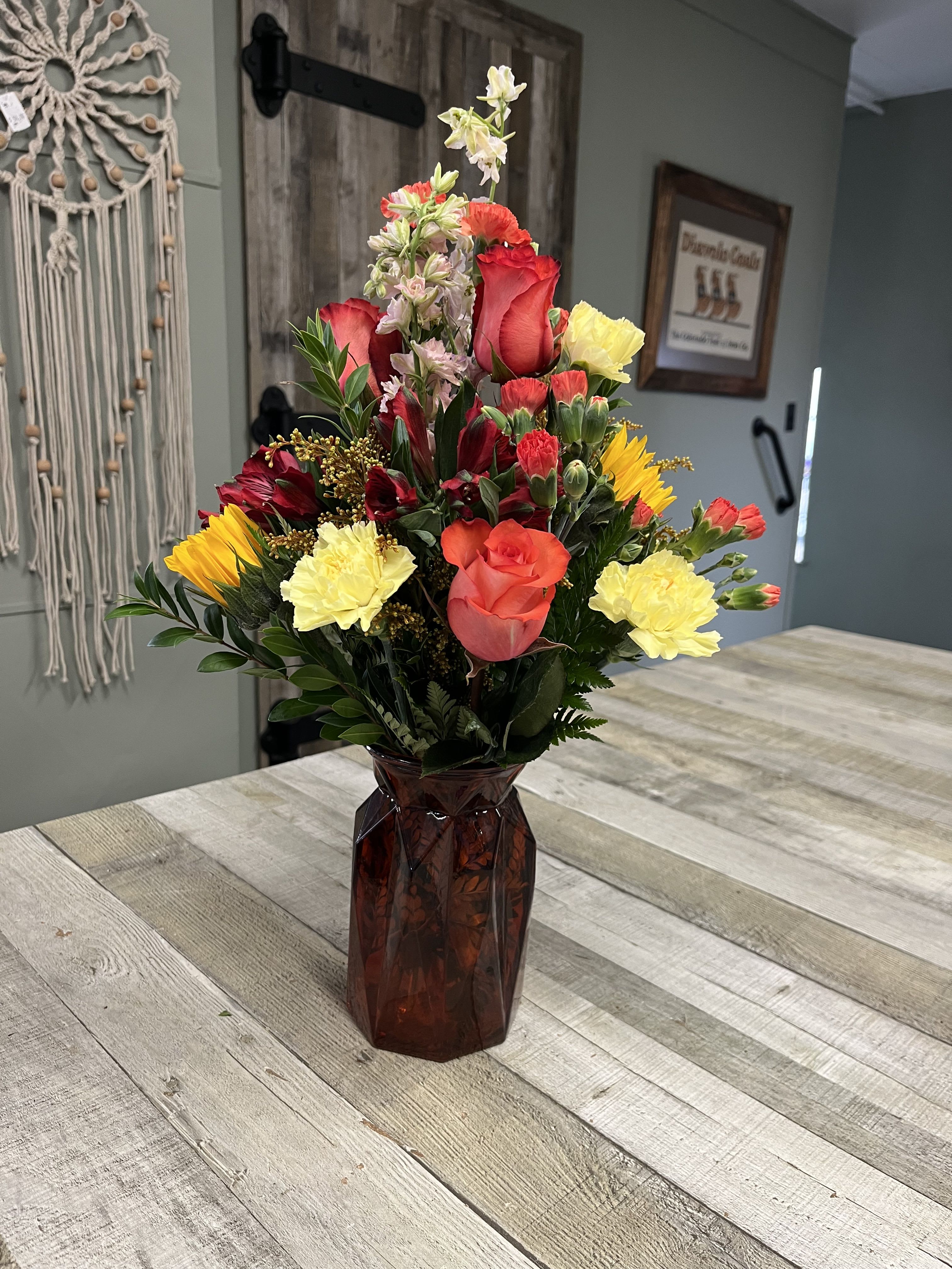 Mixed bouquet of red, yellow, and pink flowers in a dark glass vase