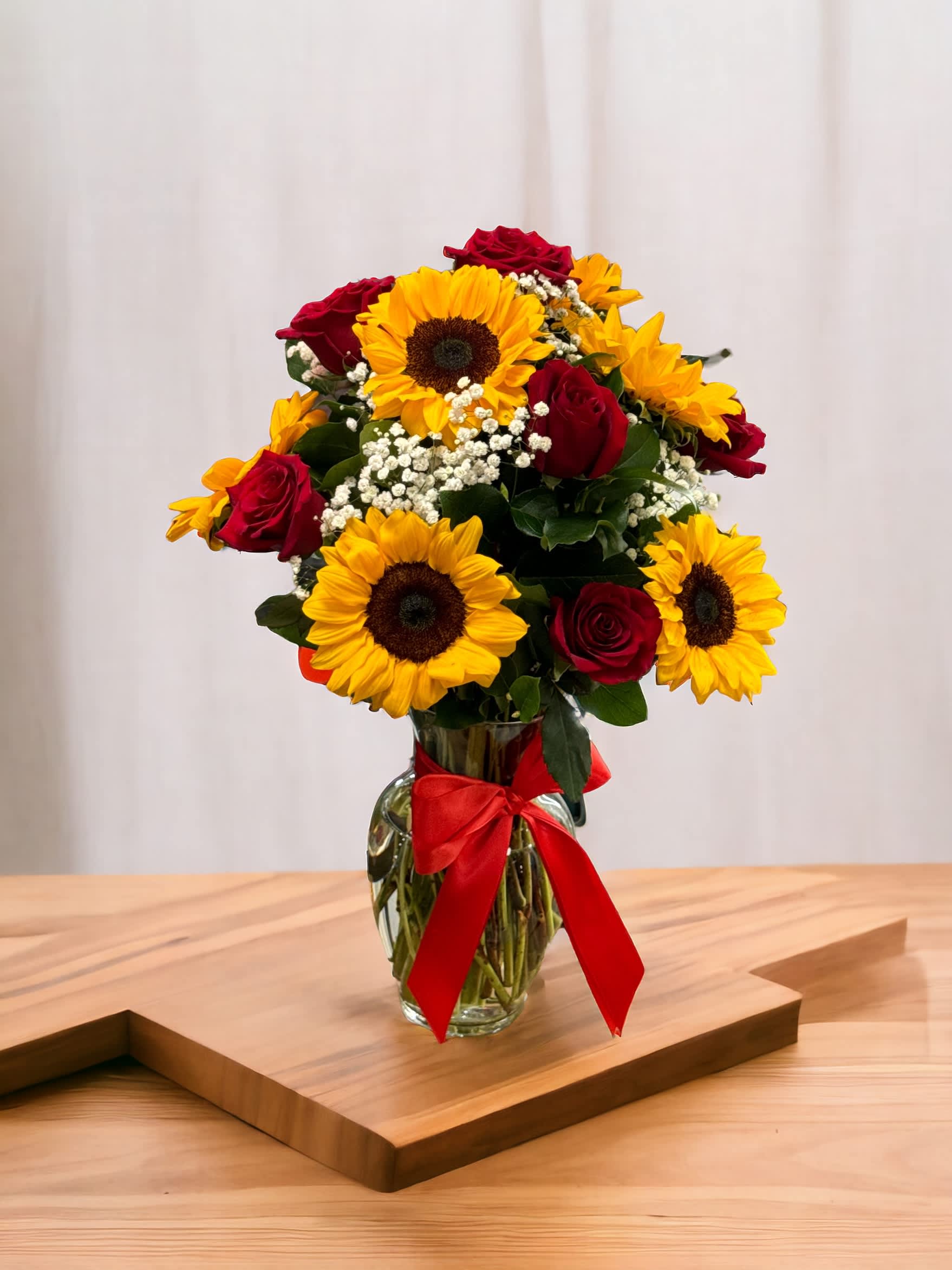Bouquet of red roses and yellow sunflowers in a glass vase with a red ribbon