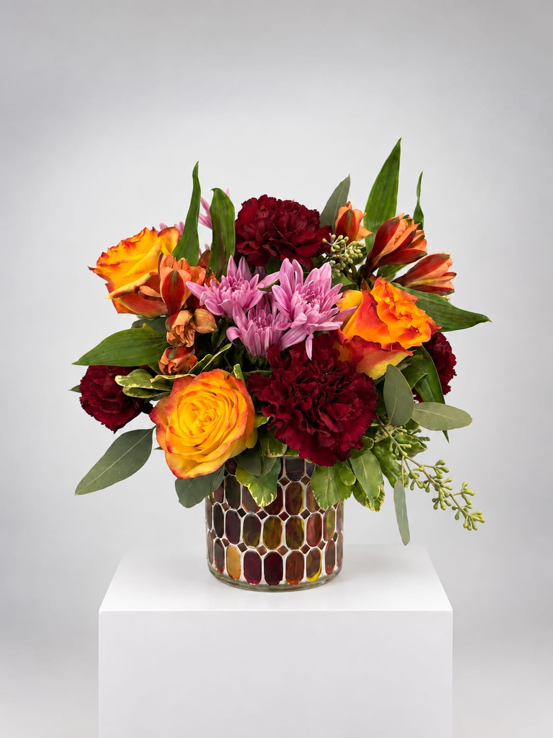 Colorful bouquet of roses, carnations, and chrysanthemums in a mosaic glass vase