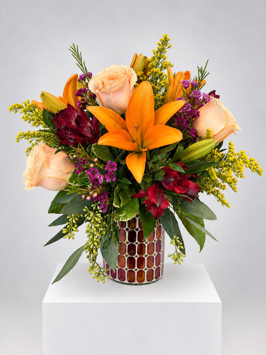 Orange lilies and peach roses in a mosaic vase