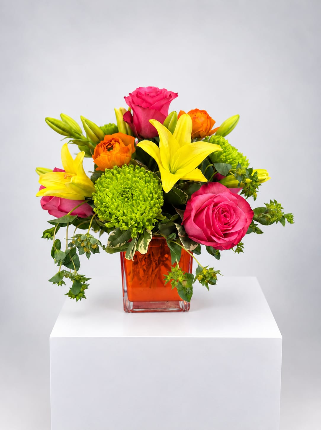 Bright mixed bouquet of roses, lilies, and green chrysanthemums in an orange vase