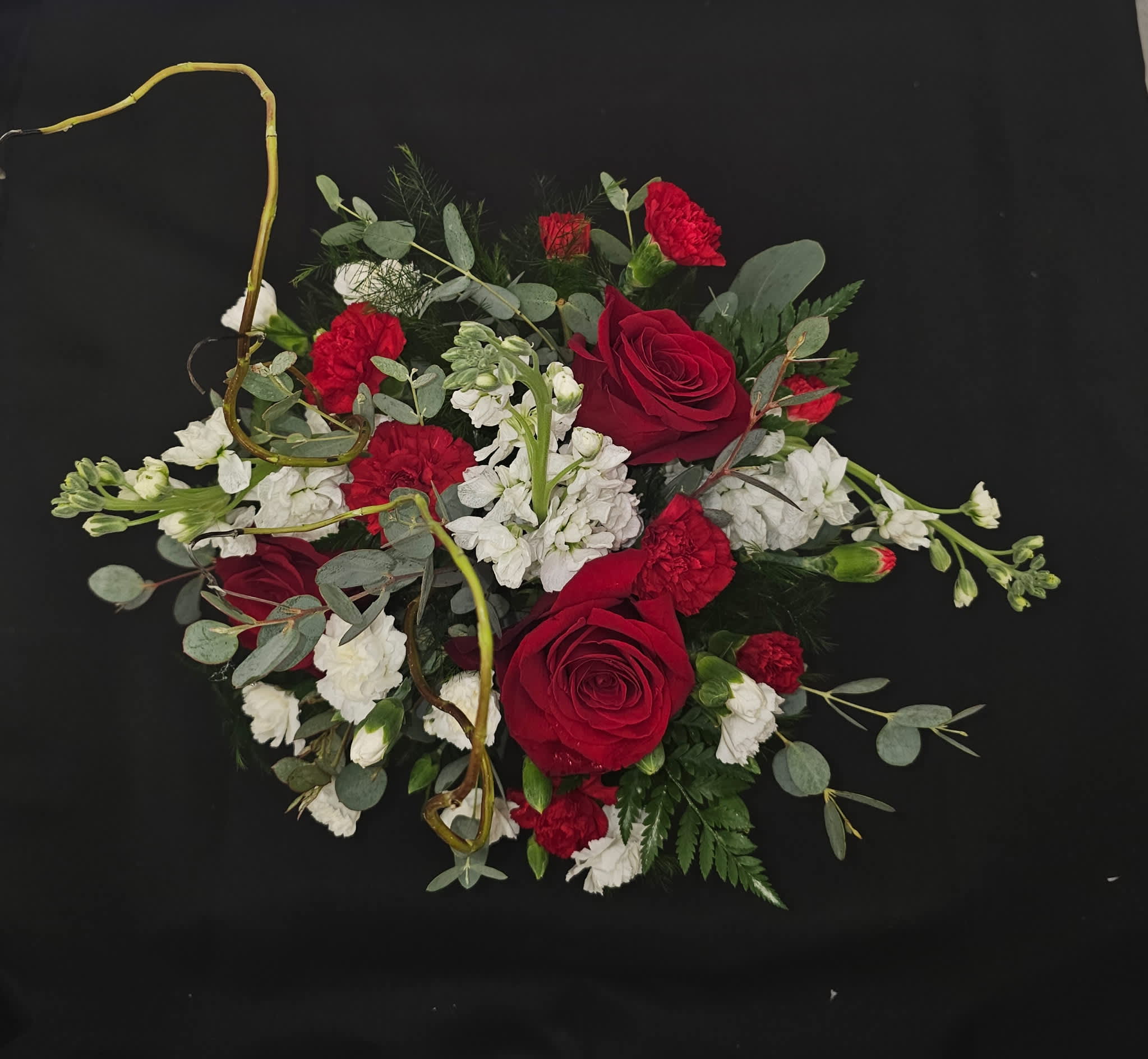 Red roses and white carnations arranged with eucalyptus on a black background