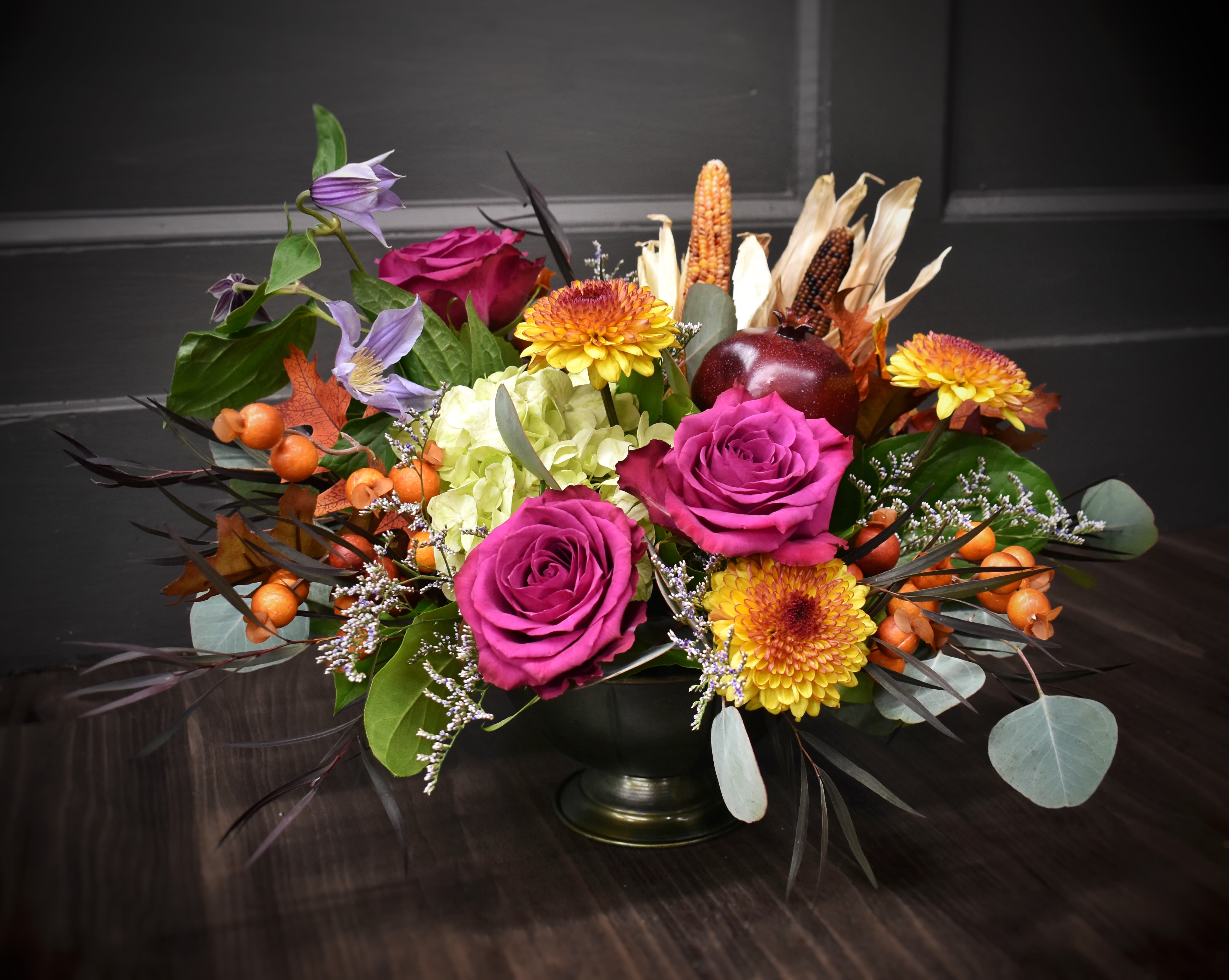 Enchanted Harvest - Everything that reminds us of the harvest season, all in one luxurious compote. This arrangement is overflowing with a mix of hydrangea, gerrondo gerbera daisies, roses, fall mums, dried corn, everlasting berries and a faux pomegranite.