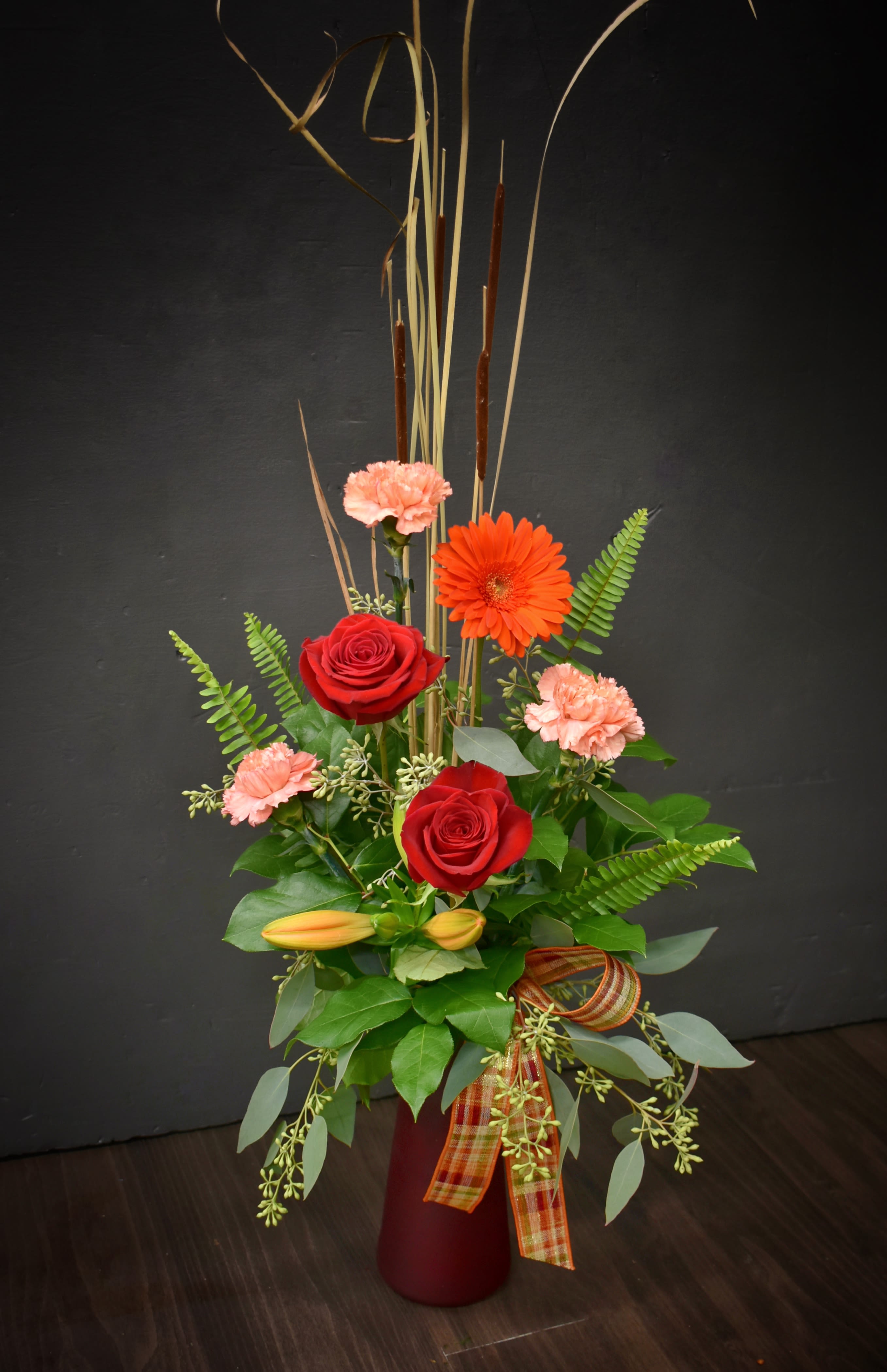 Tall red and peach floral arrangement in a burgundy vase with ribbon