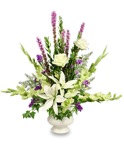 Tall white and purple floral arrangement with lilies and roses in a white pedestal vase