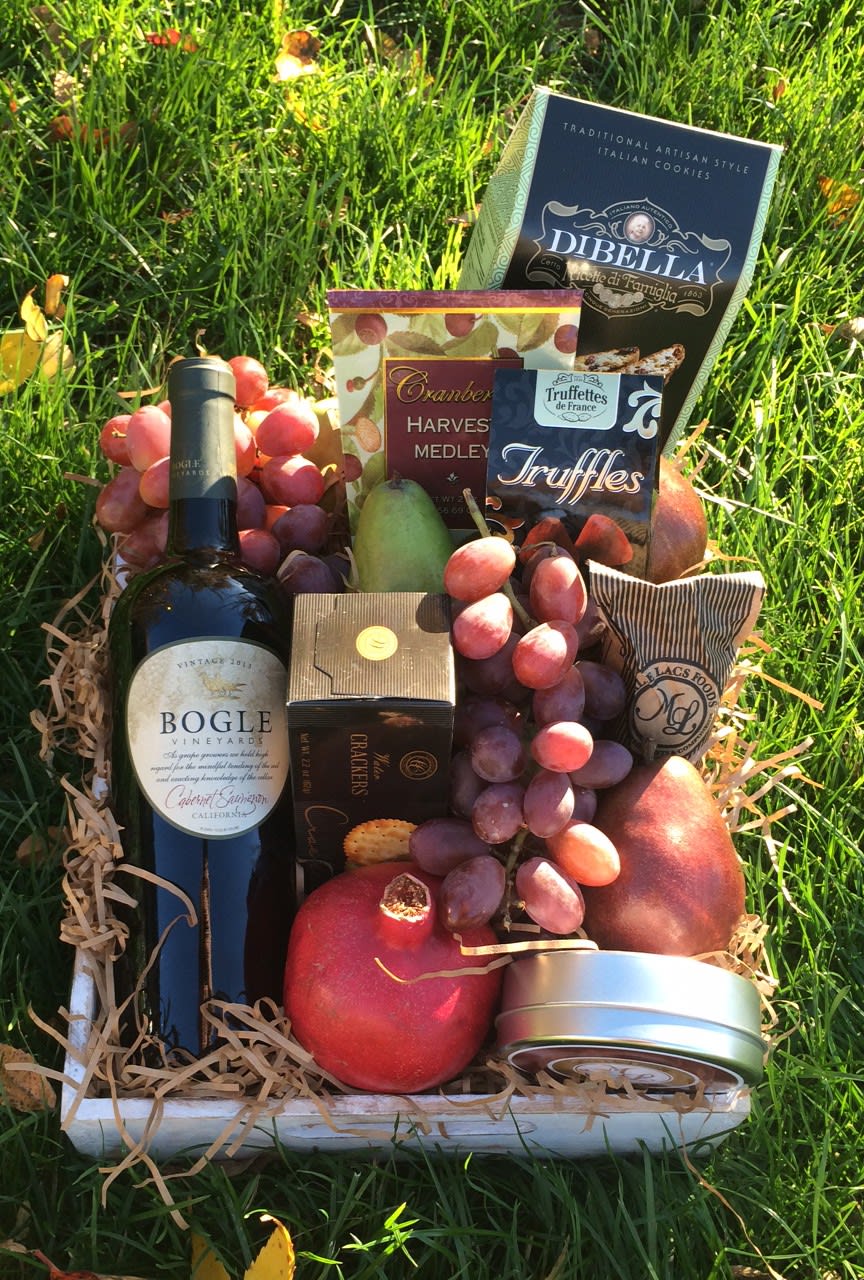 Gift basket with wine, fruit, and snack boxes on grass