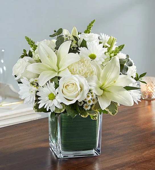White lilies and daisies arranged in a square glass vase