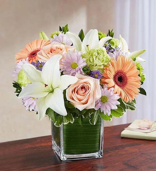 Mixed bouquet of lilies, roses, and daisies in a square glass vase