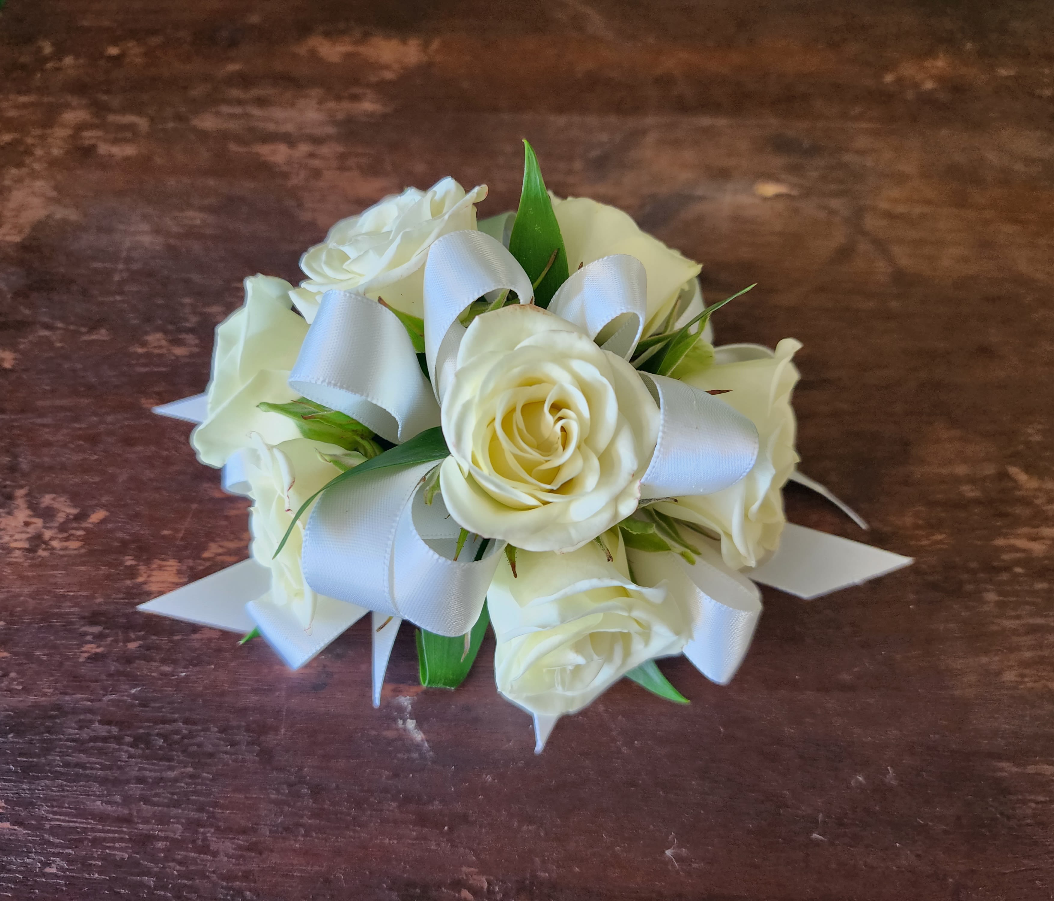 Small bouquet of white roses with white ribbon on a wooden surface