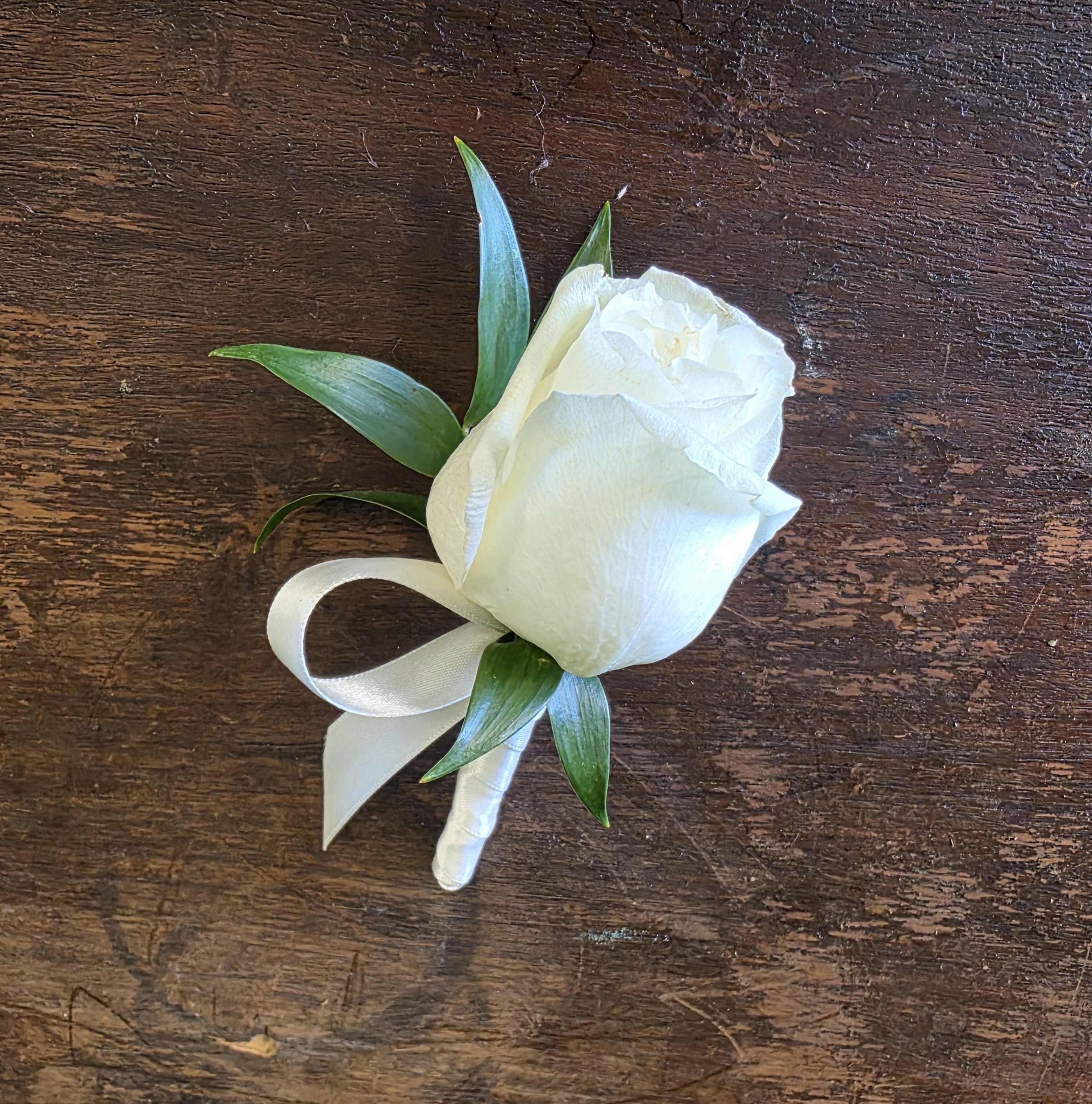White rose boutonniere with green leaves and a white ribbon