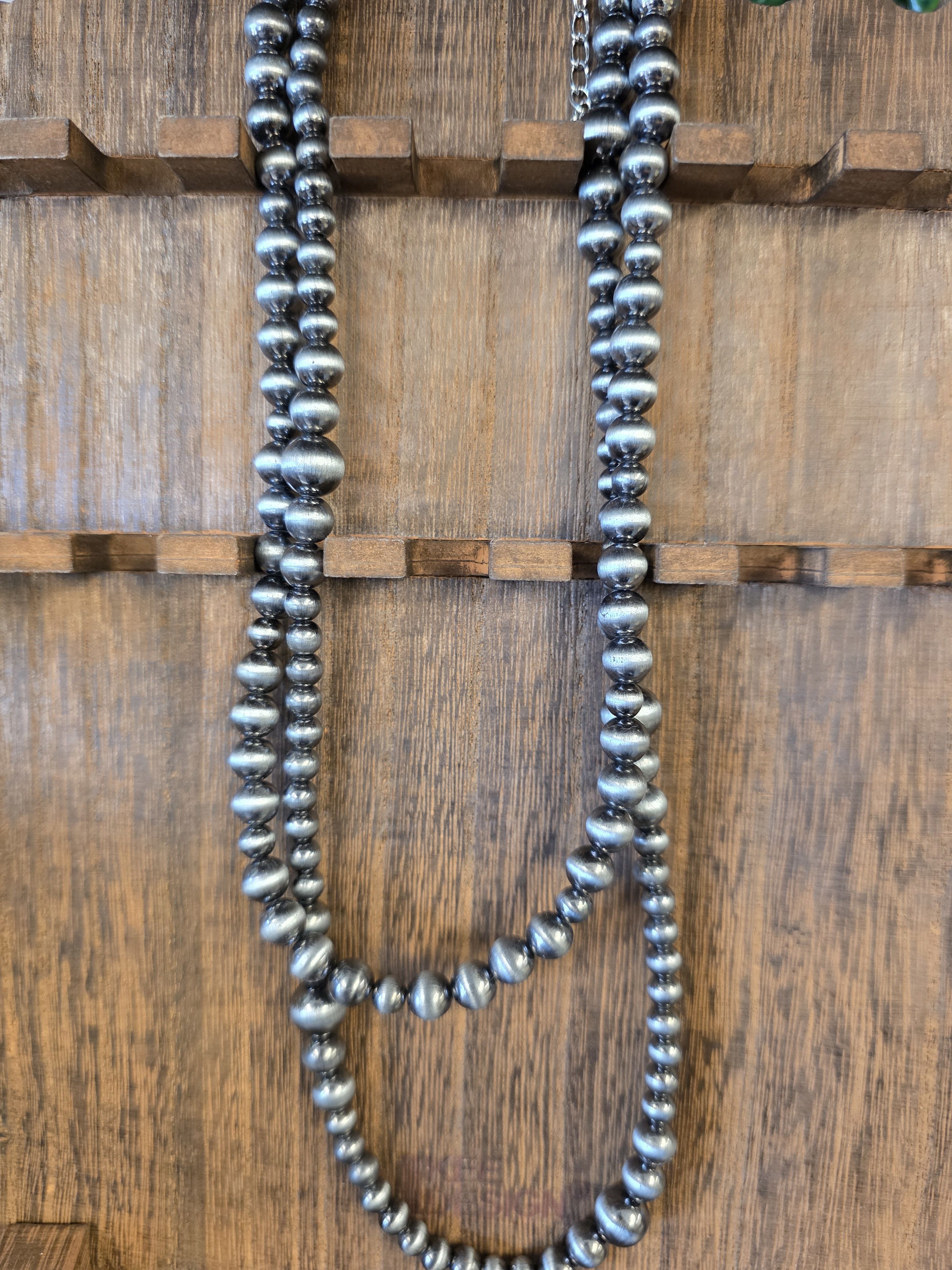 Two strands of metallic silver beads hanging on a wooden surface