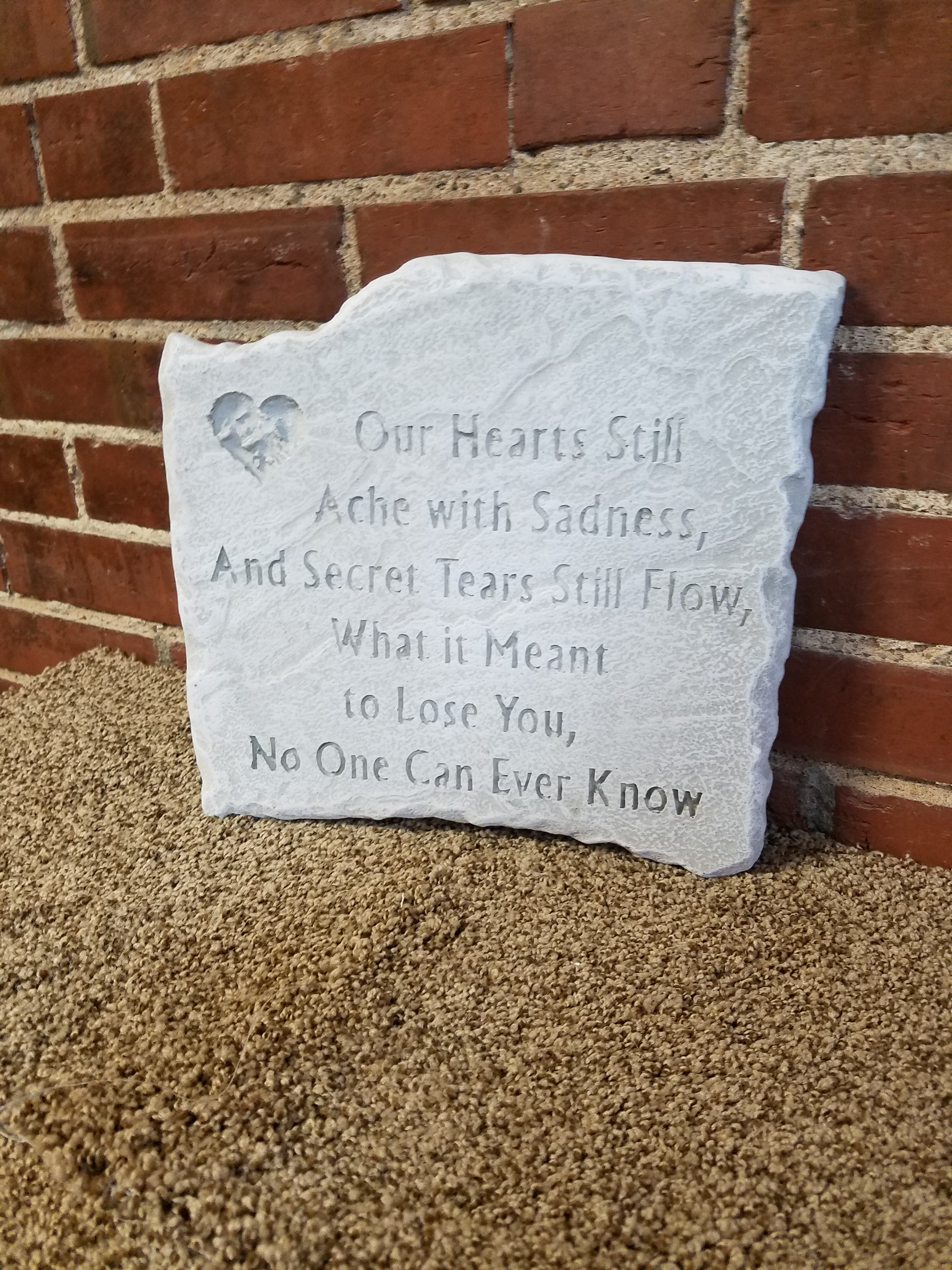 White memorial plaque with an engraved sympathy poem leaning against a brick wall