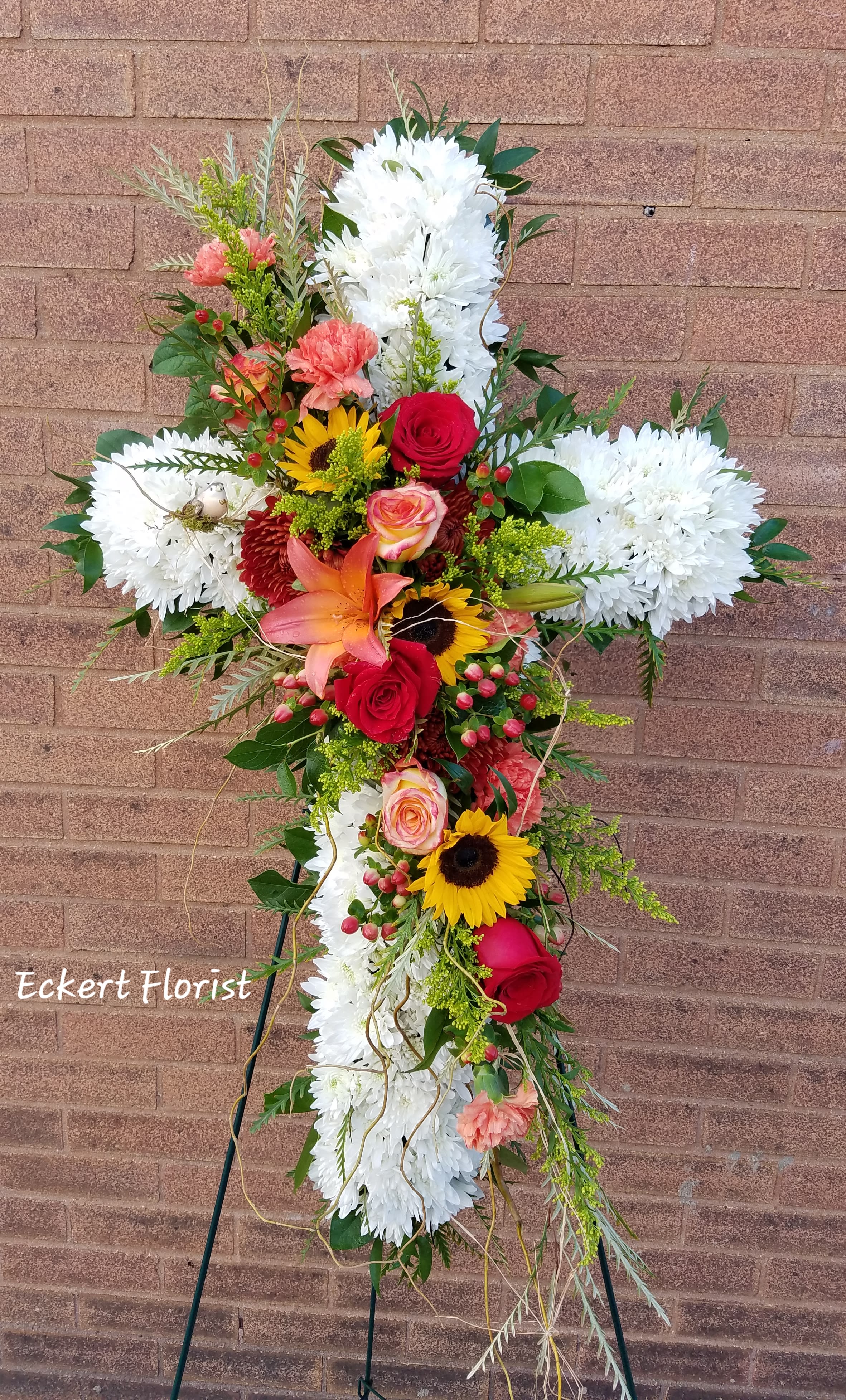 Standing floral cross with white chrysanthemums, red roses, and sunflowers