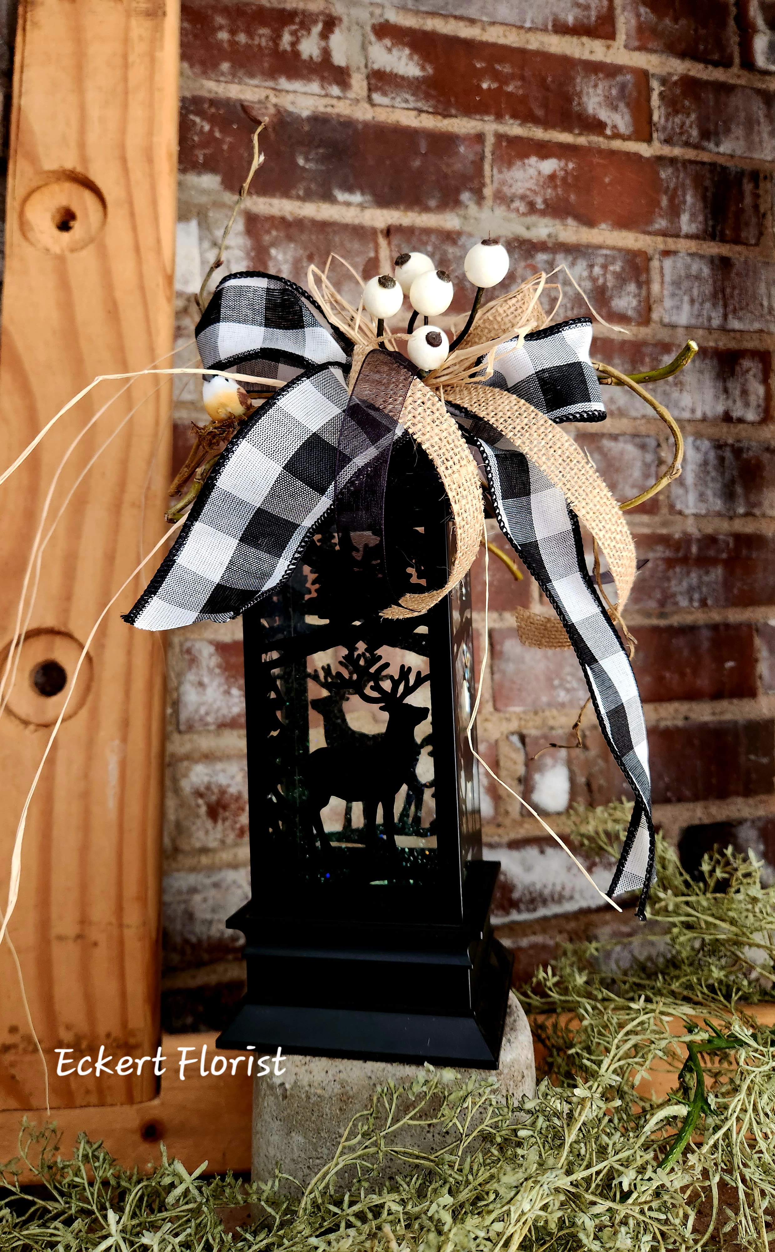 Black lantern with deer cutout topped by a plaid bow and white berries