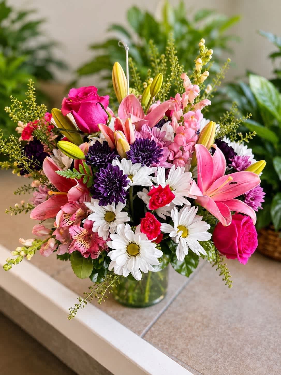 Mixed bouquet of pink lilies, roses, daisies, and purple blooms in a glass vase