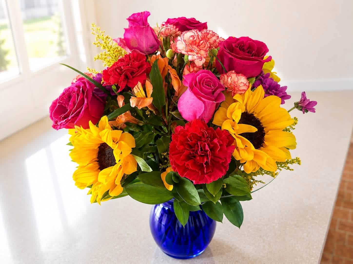 Mixed bouquet of roses, sunflowers, and carnations in a blue glass vase