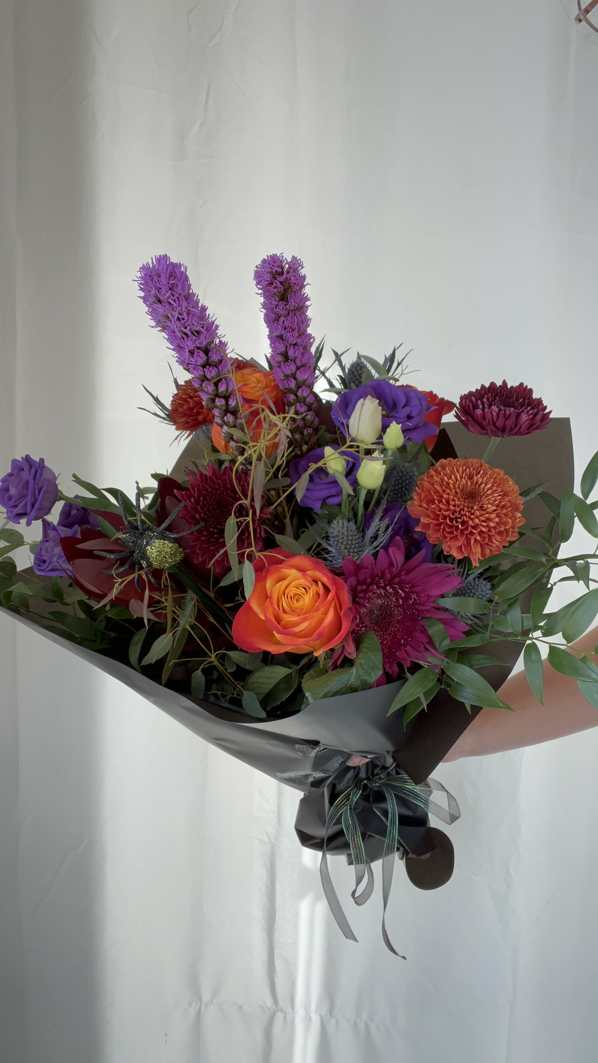 Mixed bouquet with orange and purple flowers wrapped in dark paper
