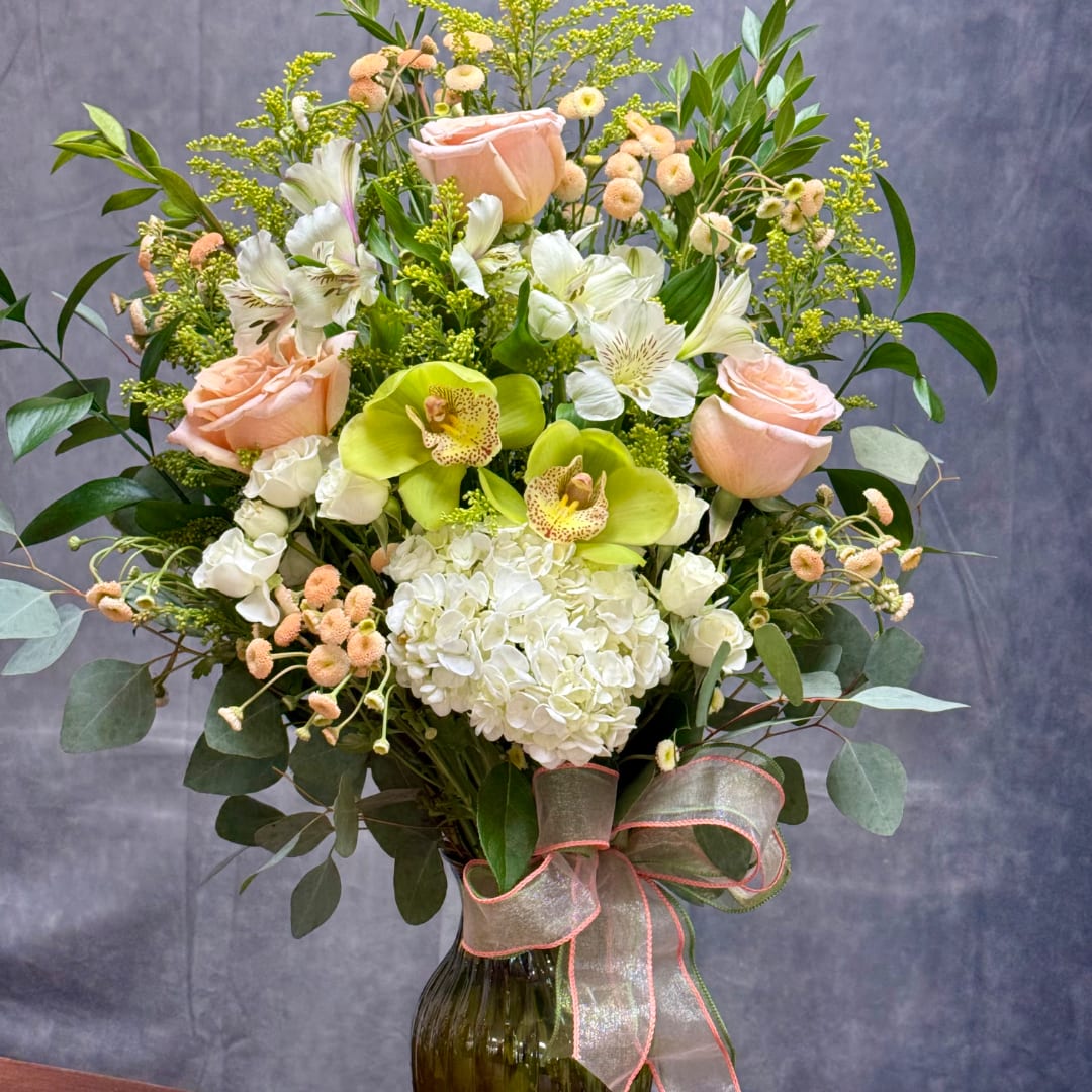 Peach roses, white hydrangea, and green orchids in a glass vase with ribbon