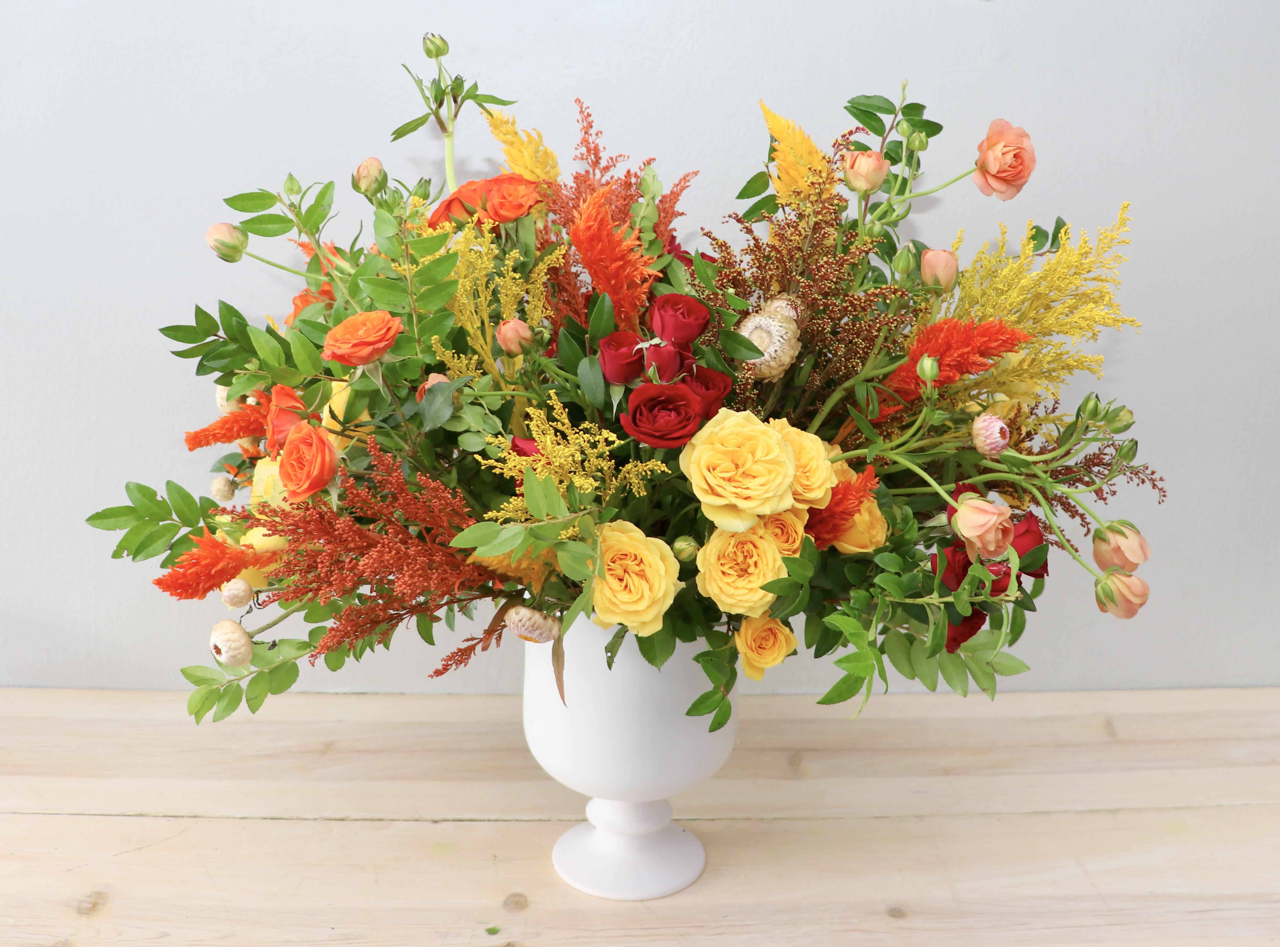 Colorful bouquet of roses and mixed blooms in a white pedestal vase