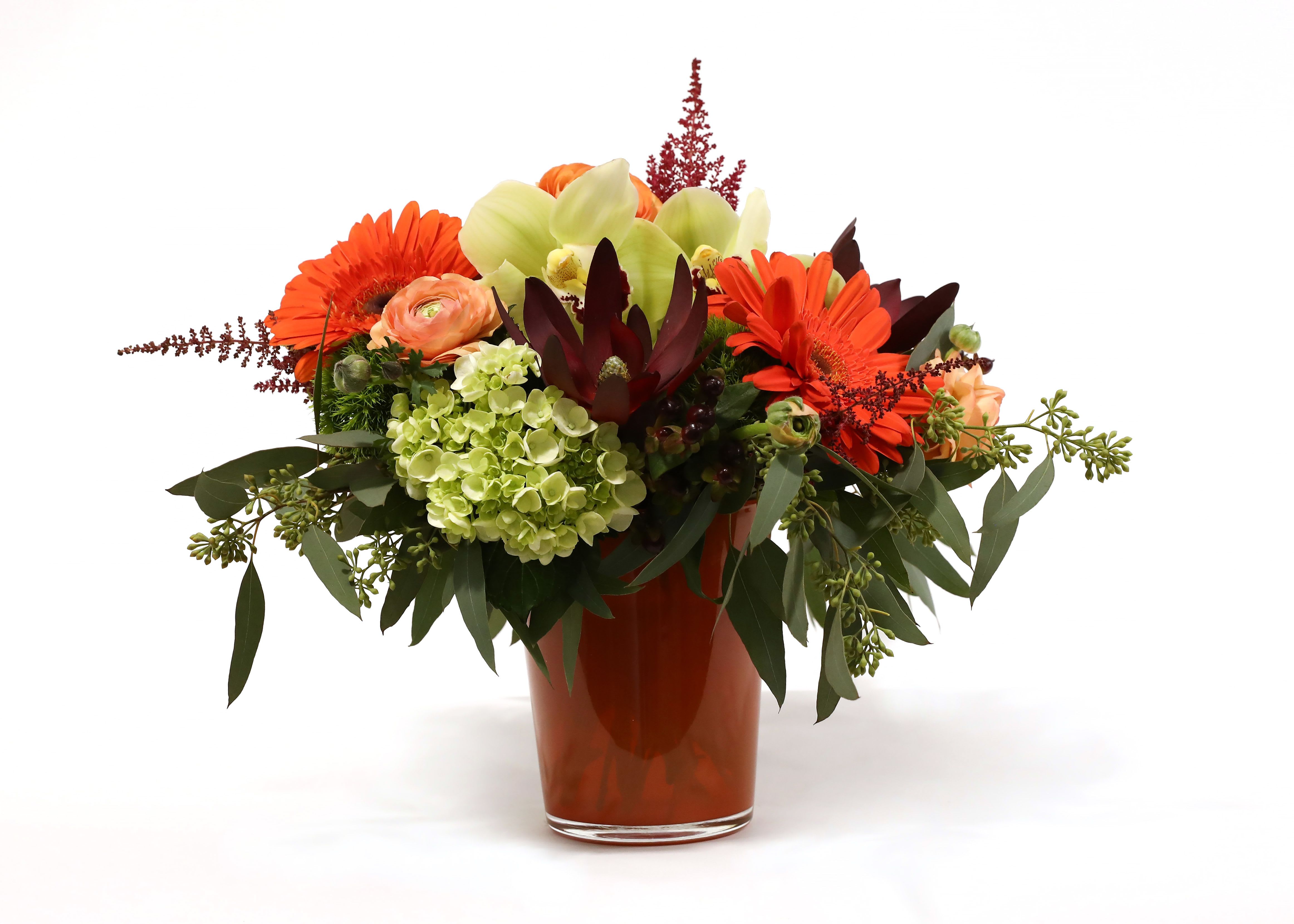 AUTUMN HARMONY  - THIS BEAUTIFUL AUTUMN ARRANGEMENT HAS MINI GREEN HYDRANGEA, GERBERA DAISIES, SAFARI SUNSET PROTEA, CYMBIDIUM ORCHIDS, ASTILBE, RANUNCULUS, AND SEEDED EUCALYPTUS IN AN ORANGE CYLINDER VASE. 