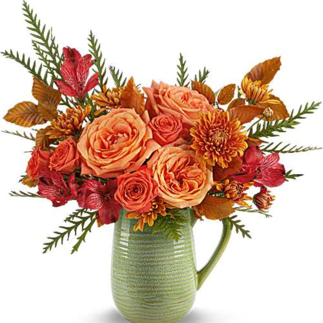 Peach and red roses in a green ceramic pitcher vase