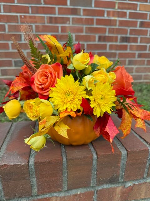 Autumn floral arrangement in a pumpkin container with yellow and orange blooms