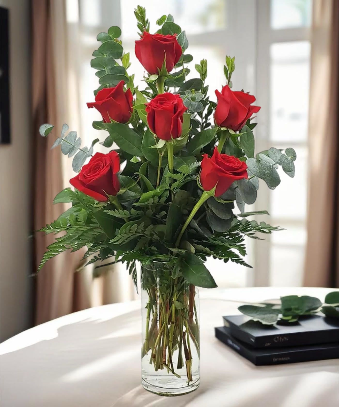 Red roses arranged in a clear glass vase with greenery
