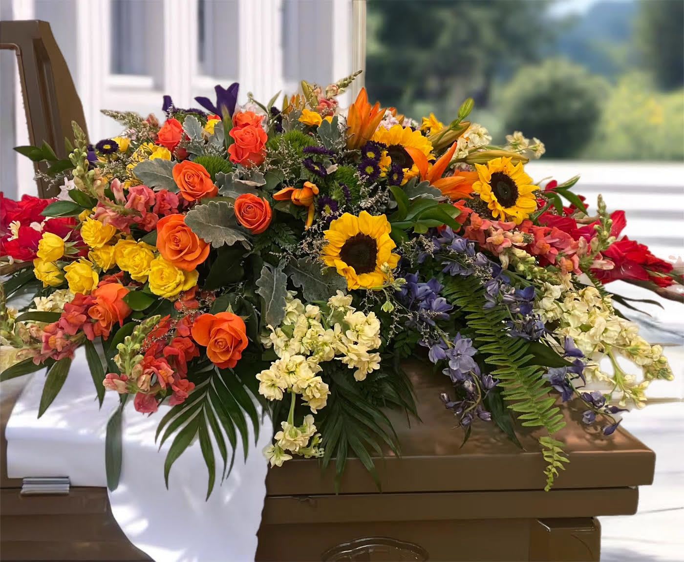 Large mixed floral casket spray with sunflowers, roses, and lilies