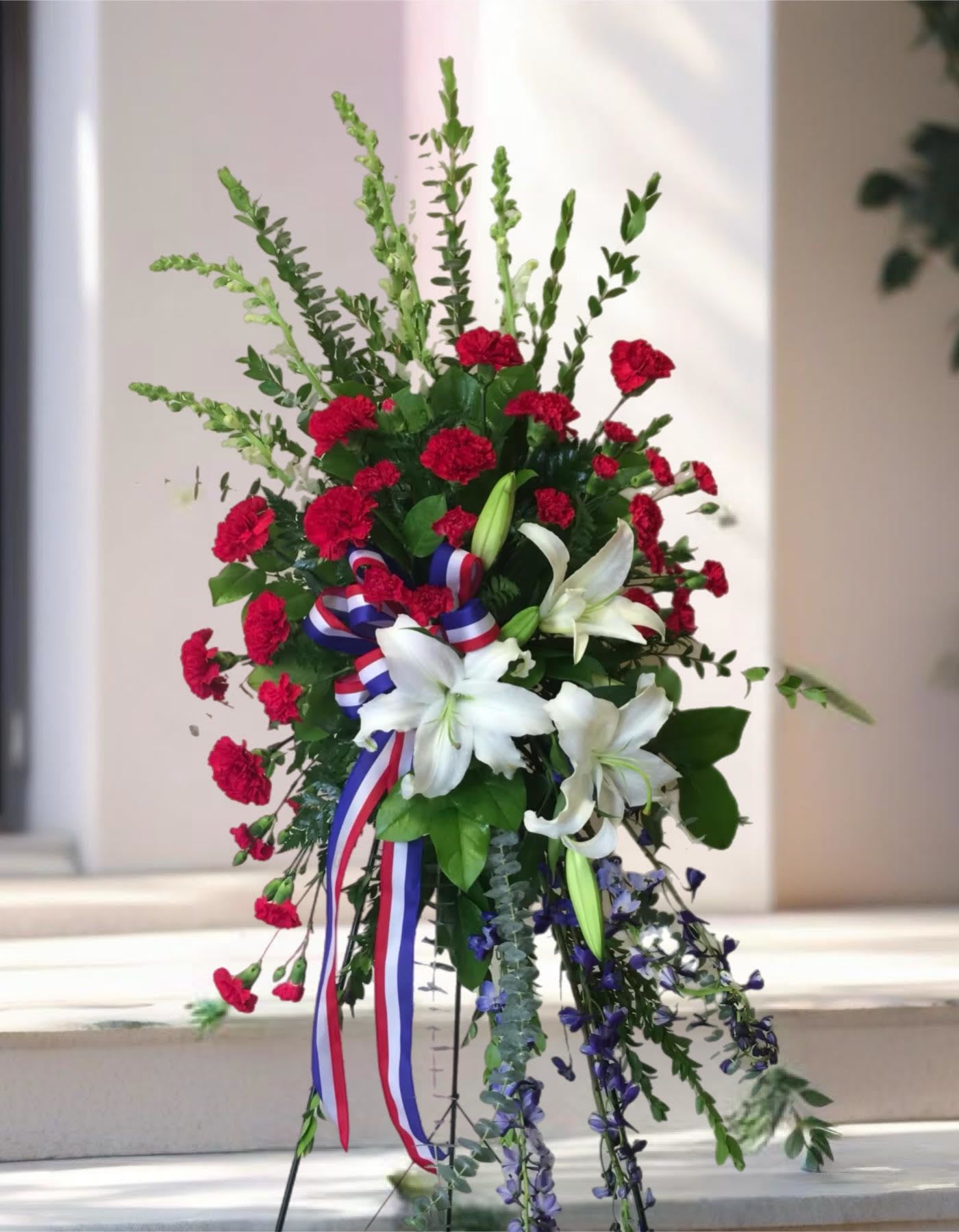 Sacred Duty Spray - Standing tall, proud and patriotic, this dazzling free-standing spray is like a fireworks display made of graceful flowers. Uniquely beautiful, it's a lovely way to honor a great loss. 