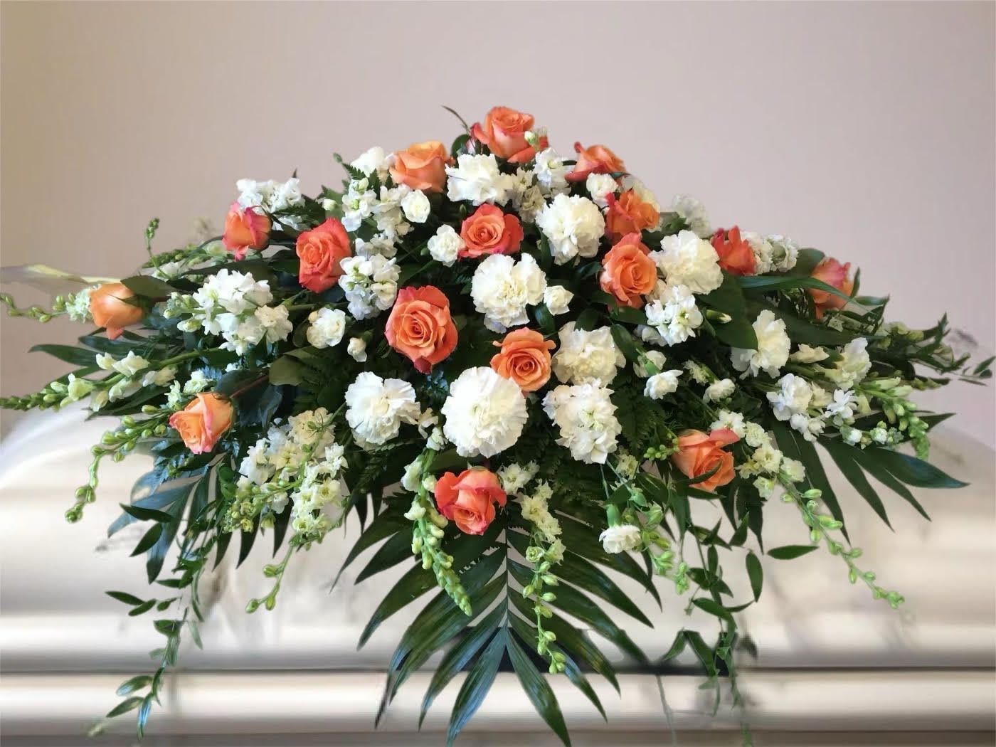 Orange and white floral casket spray with cascading greenery