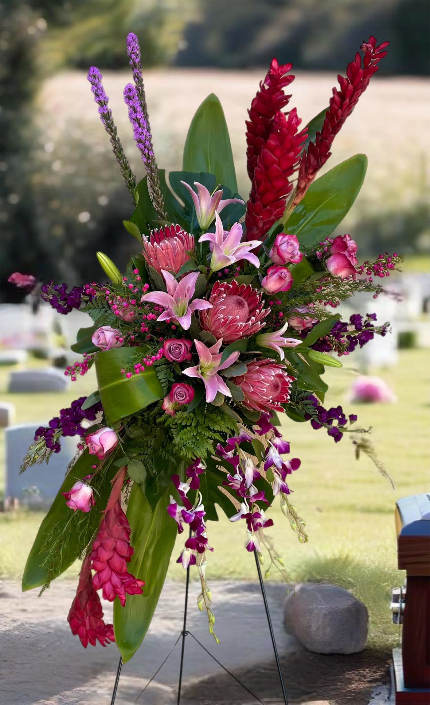 Tall tropical floral spray with pink lilies and red protea on a stand