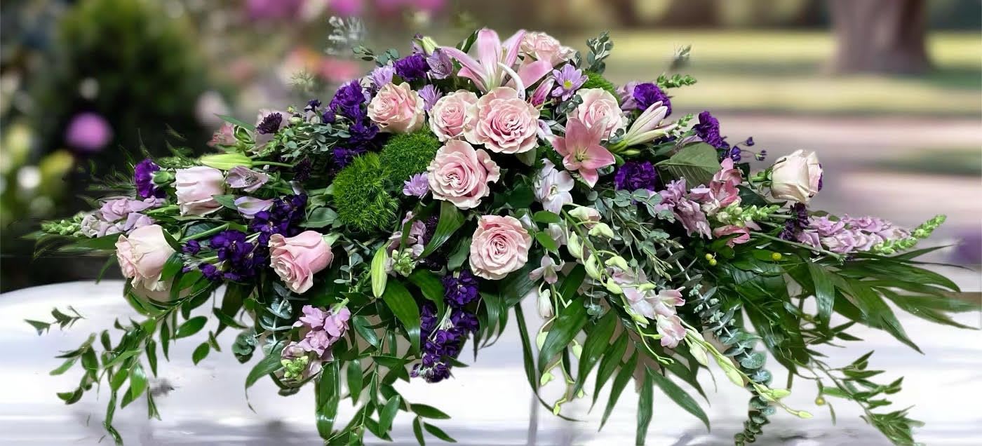 Low floral casket spray with pink roses and purple flowers