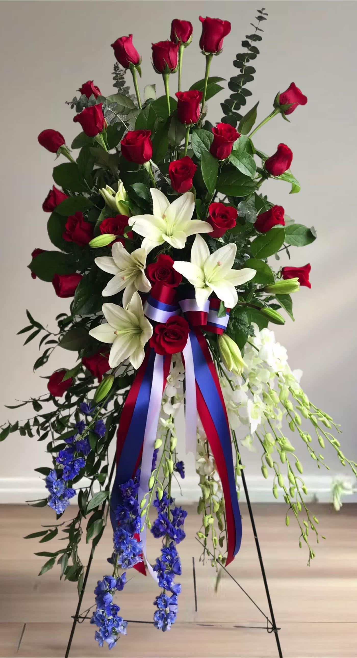 Lily and Rose Tribute Easel  - Pure white lilies and dendrobium orchids mingle with red roses, white asiatic lilies and more in this magnificent and impressive standing spray of the finest blooms. A fitting tribute for a funeral, wake or memorial service. 
