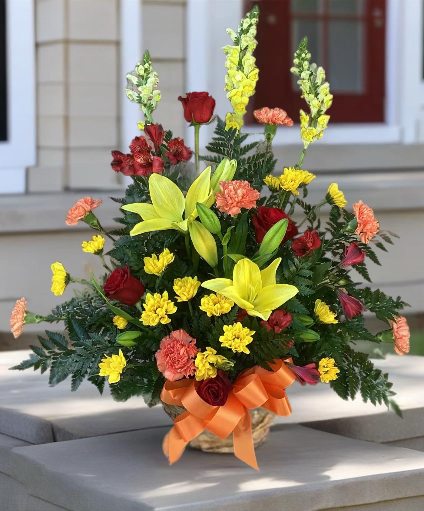 Mixed bouquet with yellow lilies, red roses, and carnations in a basket with orange ribbon