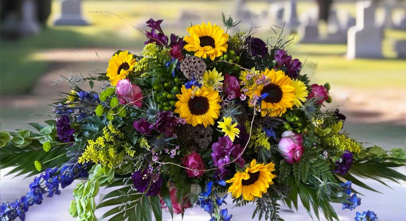 Colorful floral casket spray with sunflowers, roses, and purple blooms