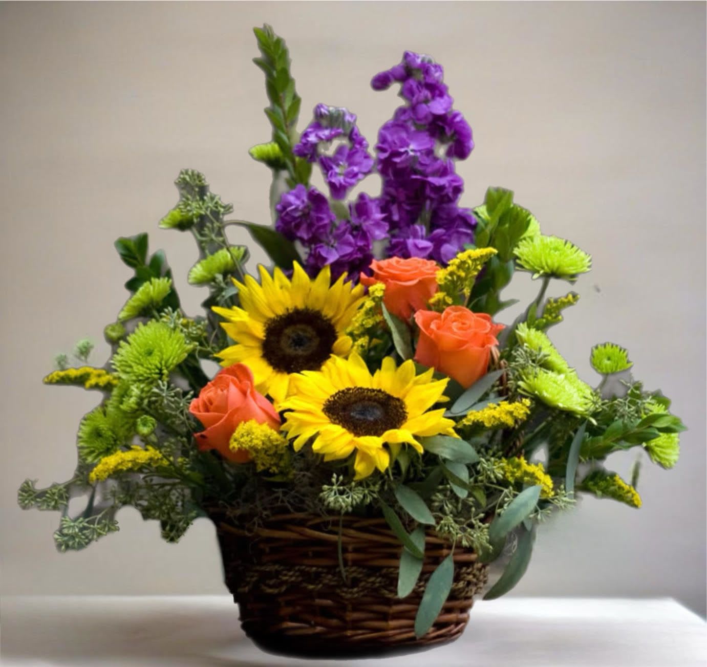 Basket arrangement with sunflowers, orange roses, and purple blooms